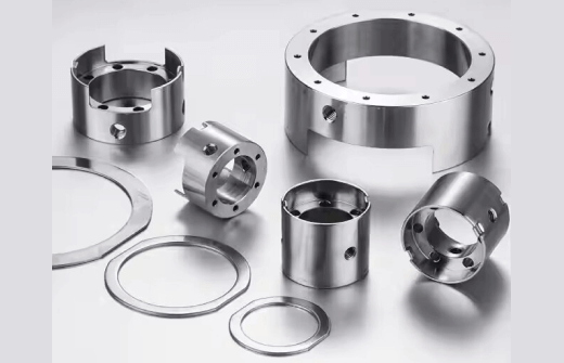 Assorted cylindrical precision-machined metal components with holes and grooves, along with metal rings